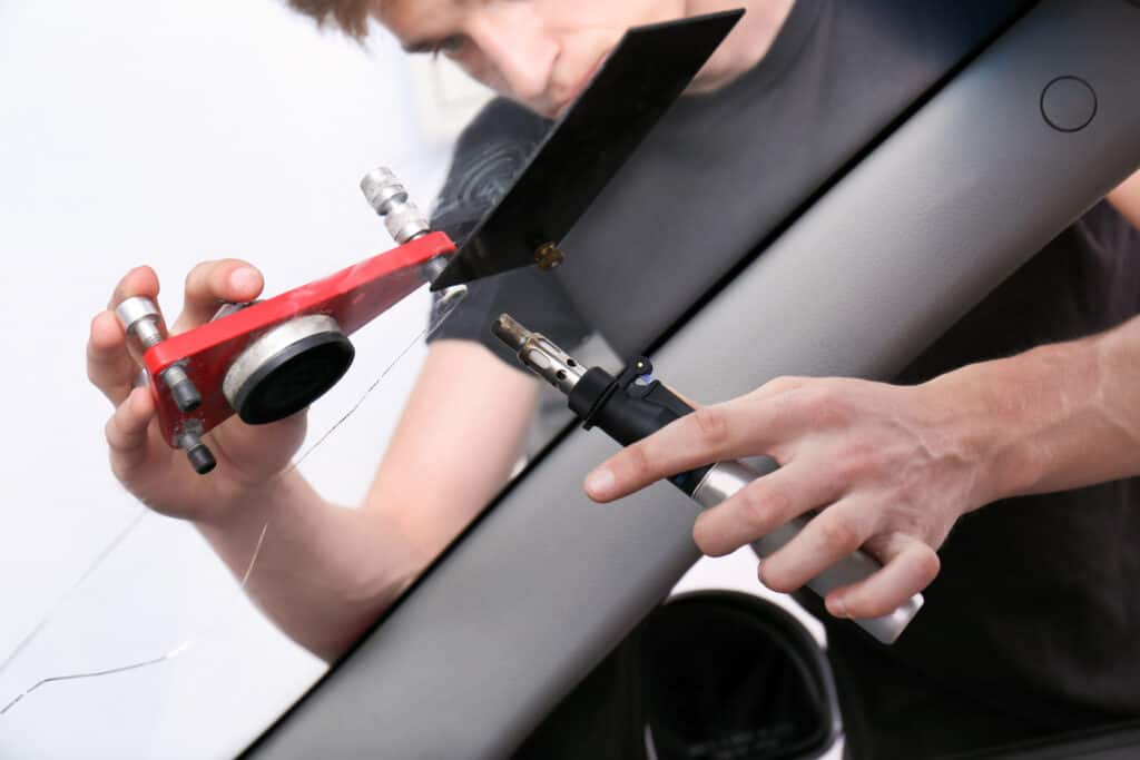 Technician fixing crack on car windshield in repair shop