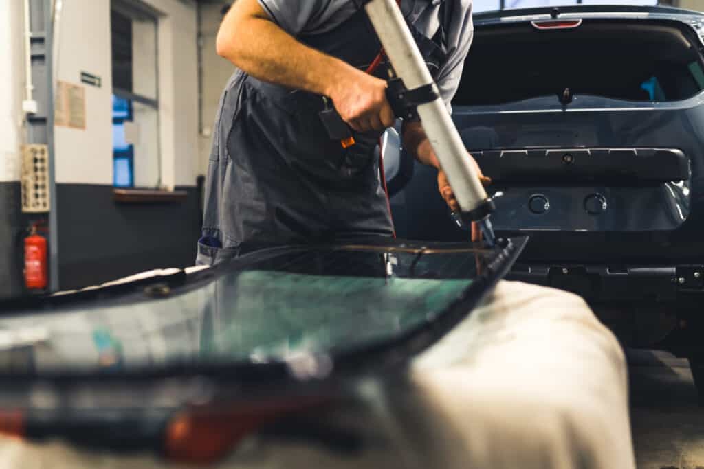 Technician adding glue to the windscreen of a car windshield replacement station